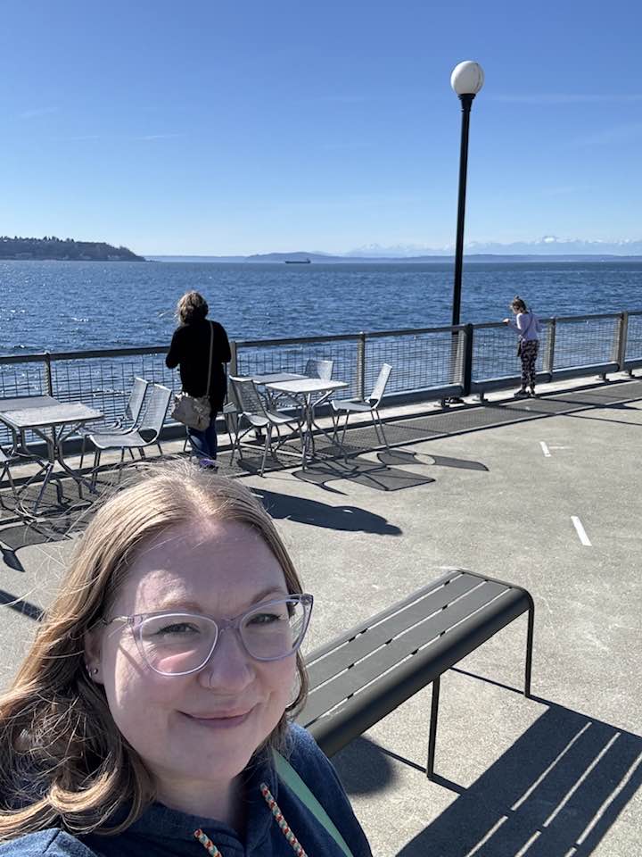 A woman faces the camera, smiling, with two kids overlooking the Seattle Sound behind her